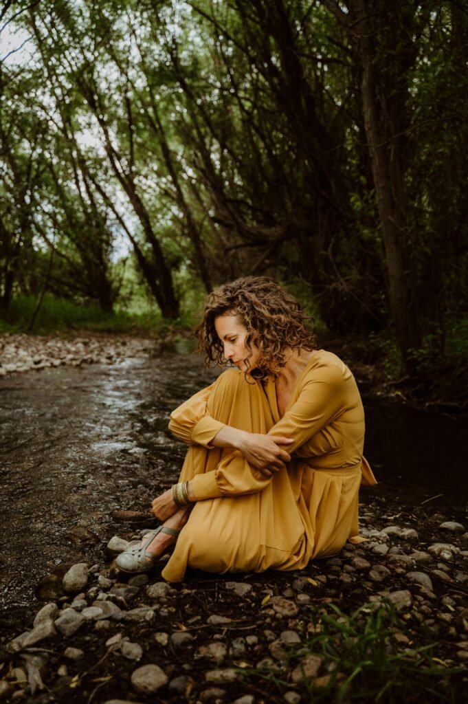Femme assise seule au bord d'une rivière, contemplant l'eau dans un moment de calme et de réflexion.