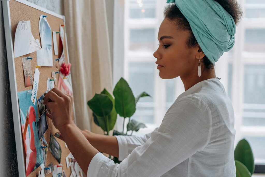 Une femme épingle des photos et images inspirantes sur un tableau mural, concentrée et apaisée.