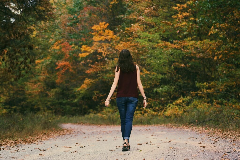 Femme marchant seule sur une bordée d'arbres, dans un environnement calme et nature.