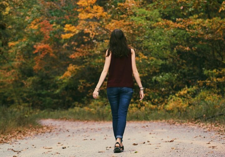 Femme marchant seule sur une bordée d'arbres, dans un environnement calme et nature.