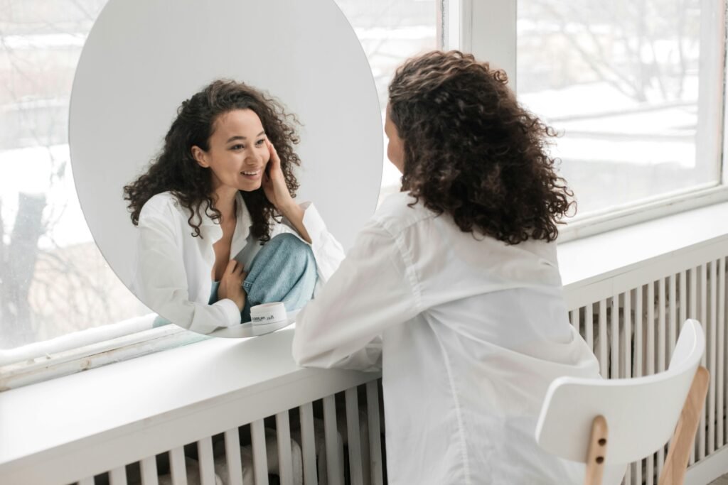 Femme souriante se regardant dans un miroir, symbolisant l'amour de soi et le recentrage personnel.