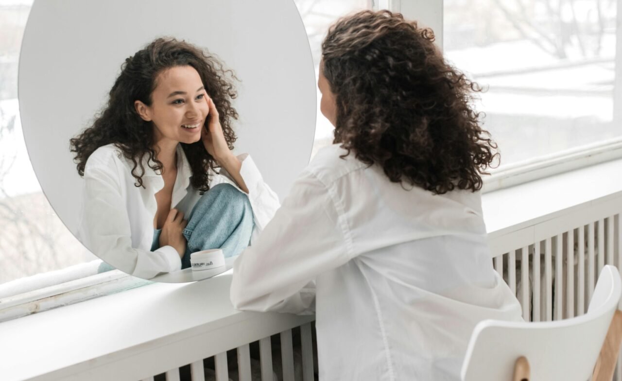 Femme souriante se regardant dans un miroir, symbolisant l'amour de soi et le recentrage personnel.