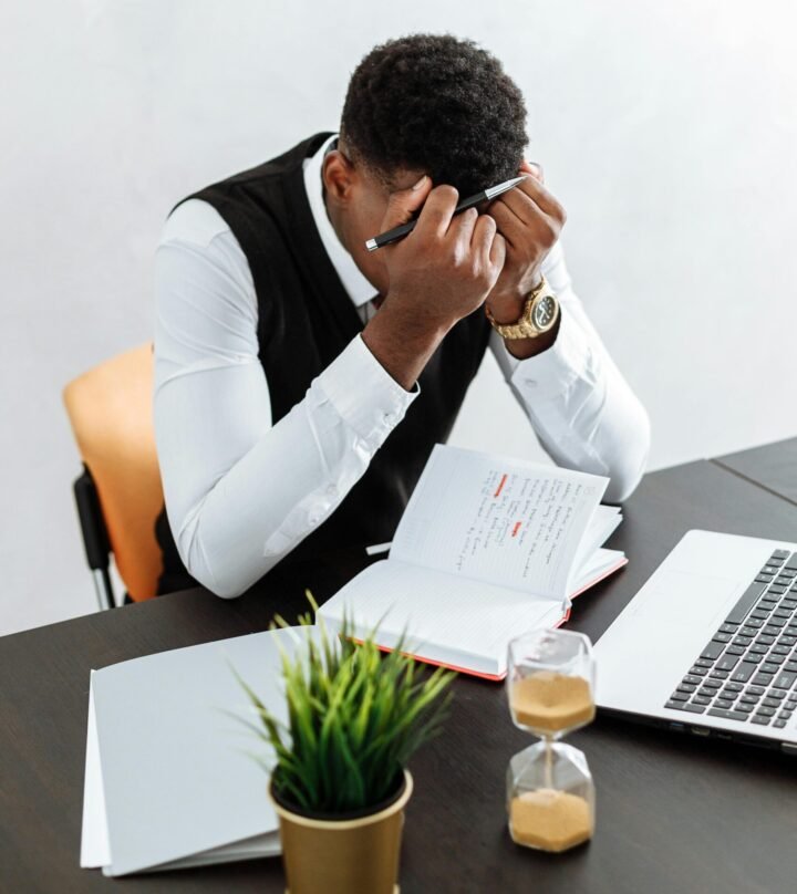 Un homme assis a son bureau, la tête dans les mains, illustrant un moment de stress intense.